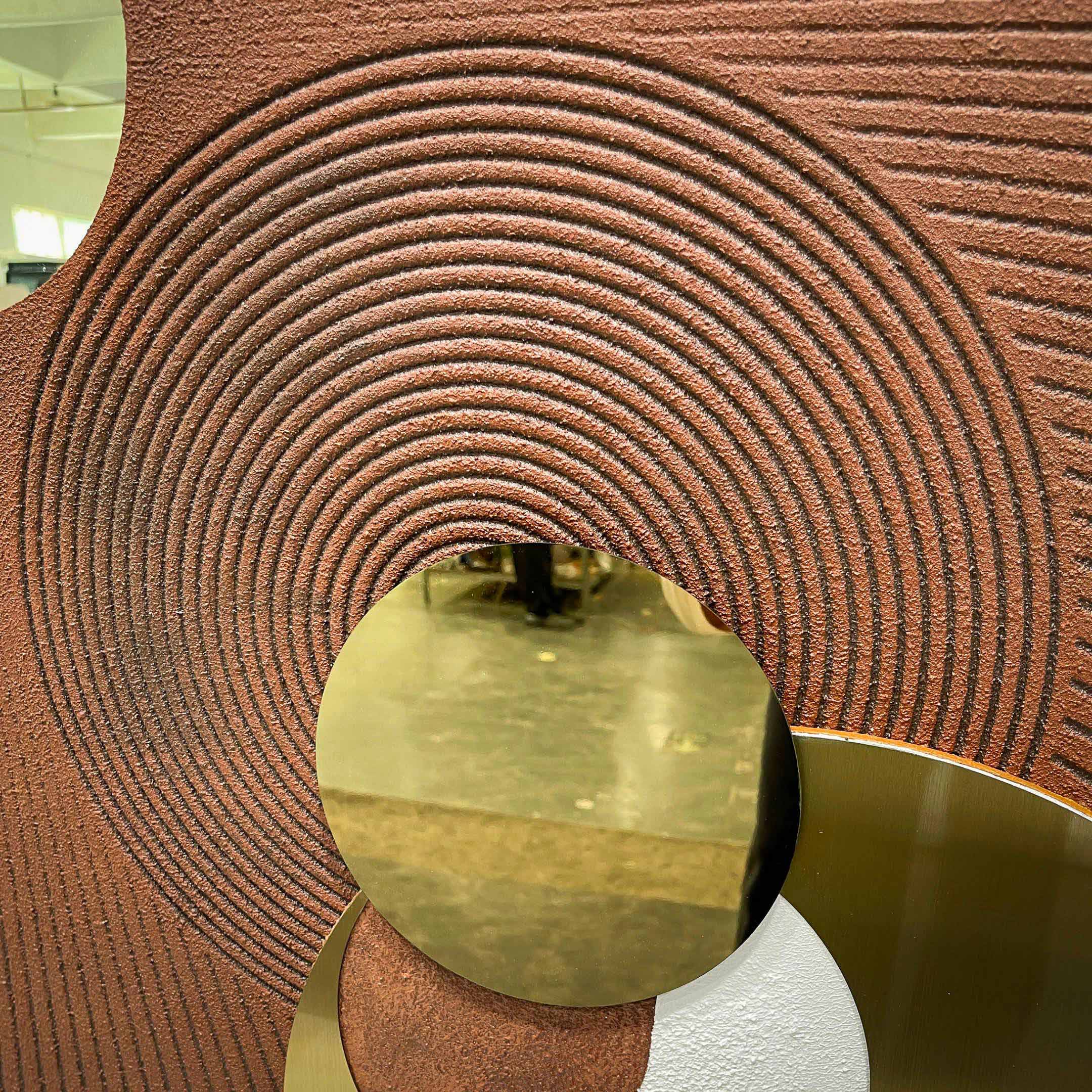 Close-up of Giant Sculptures Orbitra Copper Reflective Circular 3D Wall Art showing concentric ridged texture in warm brown around a polished copper-gold mirrored disc.