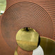 Close-up of Giant Sculptures Orbitra Copper Reflective Circular 3D Wall Art showing concentric ridged texture in warm brown around a polished copper-gold mirrored disc.