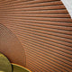 Close-up detail of the Giant Sculptures Orbitra Copper Reflective Circular 3D Wall Art showing the hand-textured warm brown panel with curved linear grooves.