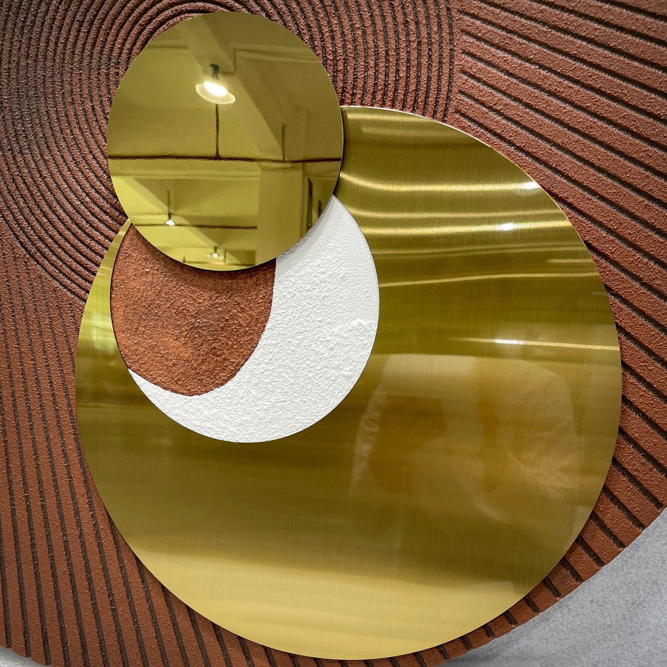Orbitra Copper Reflective Circular 3D Wall Art by Giant Sculptures, three polished gold-toned mirrored discs in a staggered arrangement on a textured brown panel.