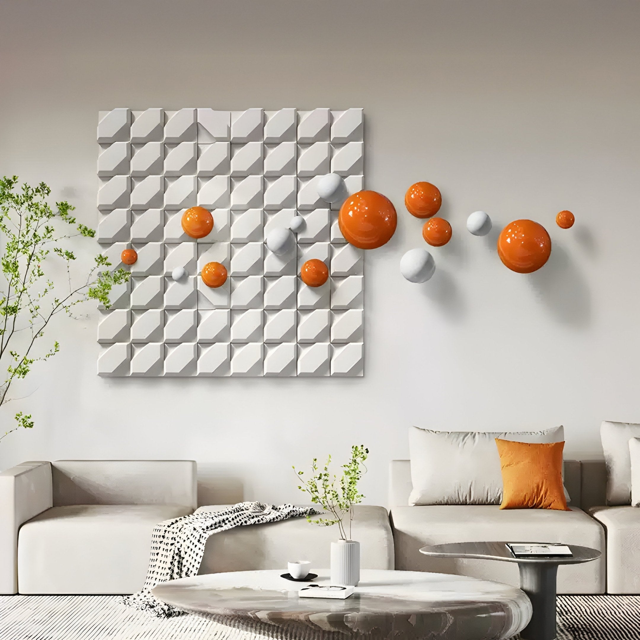 A modern living room features white sofas, a table with a plant, and the Giant Sculptures Orbina White 3D Wood Relief Wall Art With Orange & White Metal Ball on a textured wall. A gray blanket and orange pillow add pops of color to the neutral-toned space.