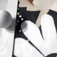 Close-up of the Florere Neutral Bloom Hand-Painted Sandstone 3D Wall Art by Giant Sculptures, featuring black, white, and beige patterns with a large soft-edged white shape on a black background. A textured white sphere casts a shadow on a light surface nearby.