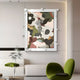 A modern living room features the Giant Sculptures Florere Vibrant Bloom Hand-Painted Sandstone 3D Wall Art with earthy tones. Below, a white couch with green pillows complements a unique hand-painted chair and a small glass table with a delicate plant enhancing the botanical theme.