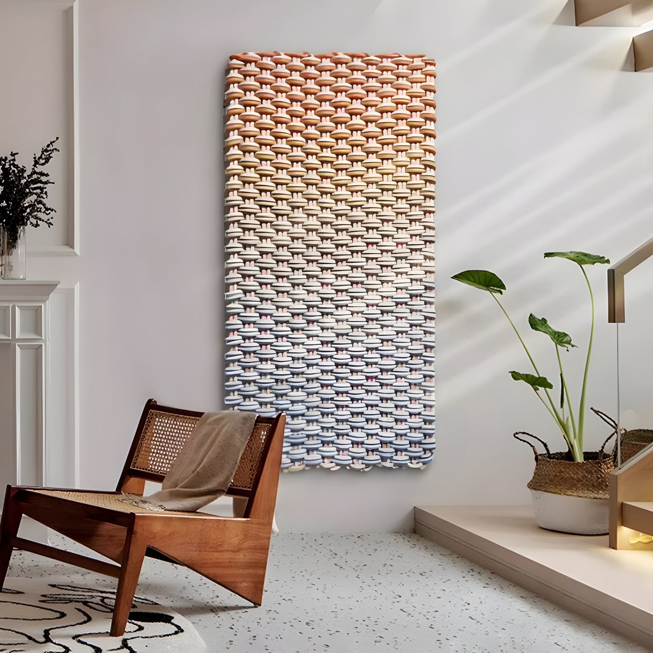 A modern room displays the Spectrum Weave Vertical Earthy Ombre Wood Relief 3D Wall Art by Giant Sculptures, featuring a color gradient from warm oranges to cool blues. A wooden chair with a woven seat sits beside a potted plant, while sunlight casts shadows on the floor and wall.