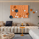 A modern living room features Orbison Terracotta 3D Wood Relief Wall Art With Floating Metal Ball by Giant Sculptures, adding sculptural décor with its textured patterns and blue, orange, and white spherical accents. The space includes a cream sectional, a round table with books, and an orange side table with a glass lamp.