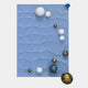 The Orbison Sky Blue 3D Wood Relief Wall Art With Metal Ball by Giant Sculptures features a blue rectangular background with layered wavy textures and scattered white, gold, blue, and dark blue spheres for a unique 3D effect.