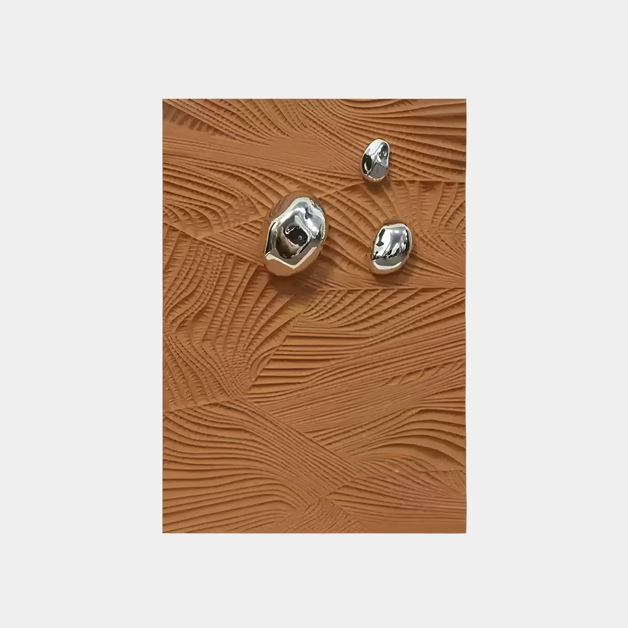 Three shiny metallic objects from the Verdara Terracotta Wood Relief 3D Wall Art by Giant Sculptures rest on a textured orange, resin-like surface with swirling patterns.