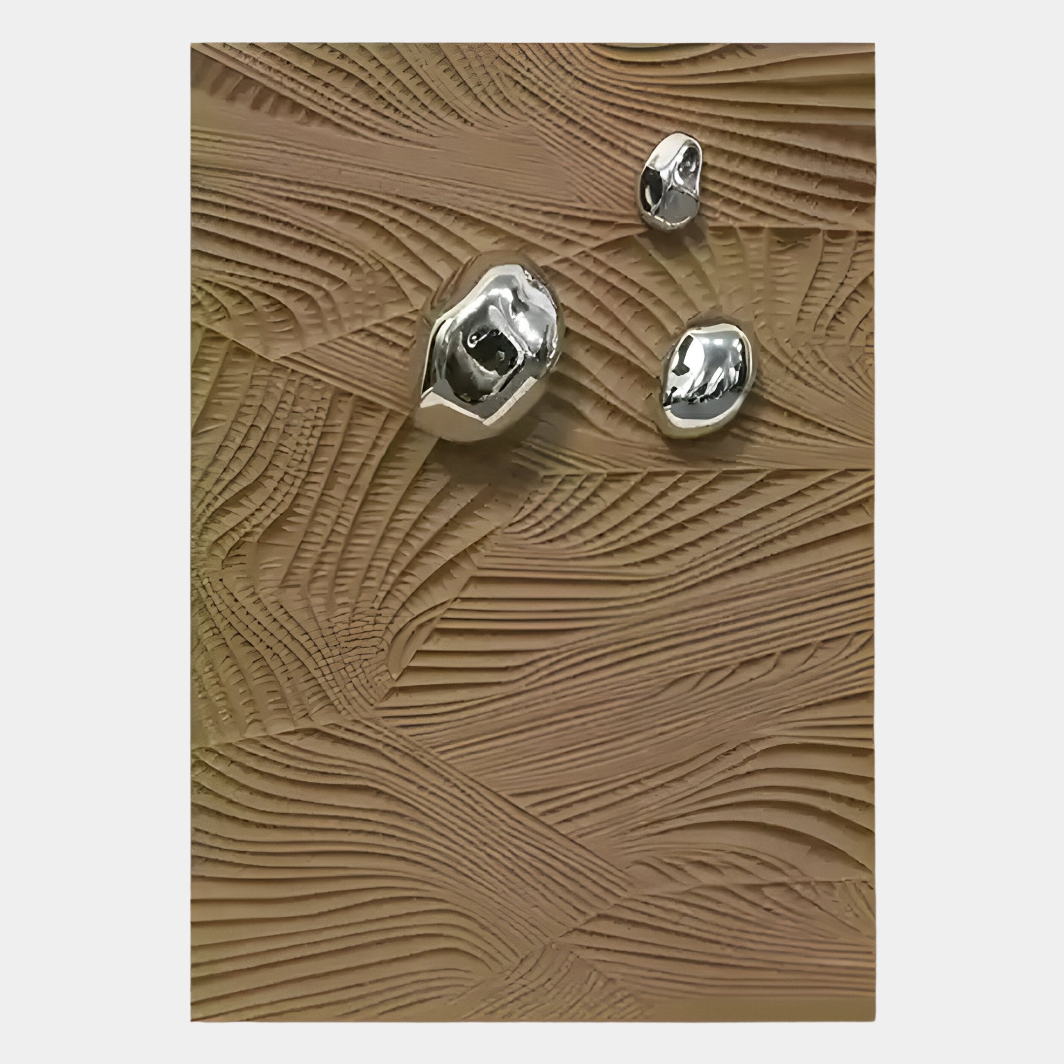 Three shiny, irregular silver objects rest on a wavy tan surface with intricate carved patterns, showcasing the earthy character of the Verdara Taupe Wood Relief 3D Wall Art by Giant Sculptures.