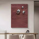 The Verdara Burgundy Red Wood Relief 3D Wall Art by Giant Sculptures boasts a textured surface with metallic spheres. Hanging above a light wood bench and two white chairs, it enhances a small minimalistic shelf holding books and a black bowl.