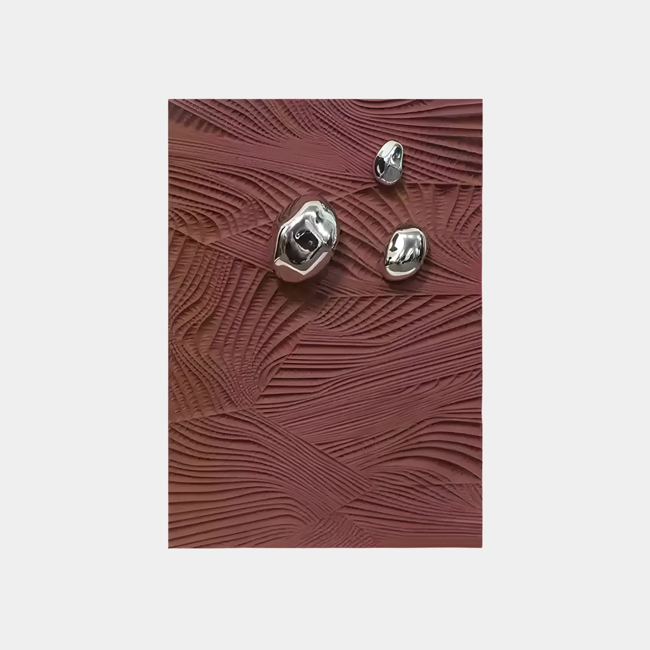 The Verdara Burgundy Red Wood Relief 3D Wall Art by Giant Sculptures features a textured surface with wave-like undulations in burgundy red. It includes three shiny, irregular metallic objects that reflect light, contrasting beautifully against the matte backdrop to create an intriguing visual effect.