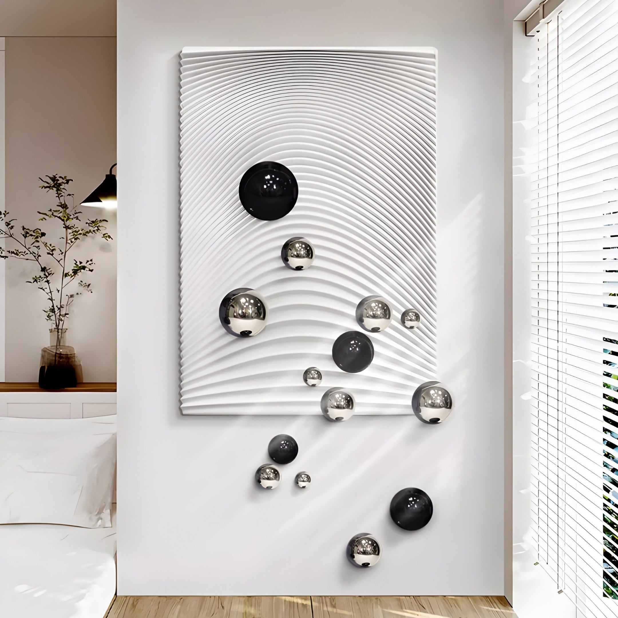 The Giant Sculptures Sphera White 3D Wood Relief Wall Art features a large white panel with swirling ripples and reflective black and silver metal balls, creating a striking 3D effect in a minimalistic room with a plant by the window and a simple white bed.