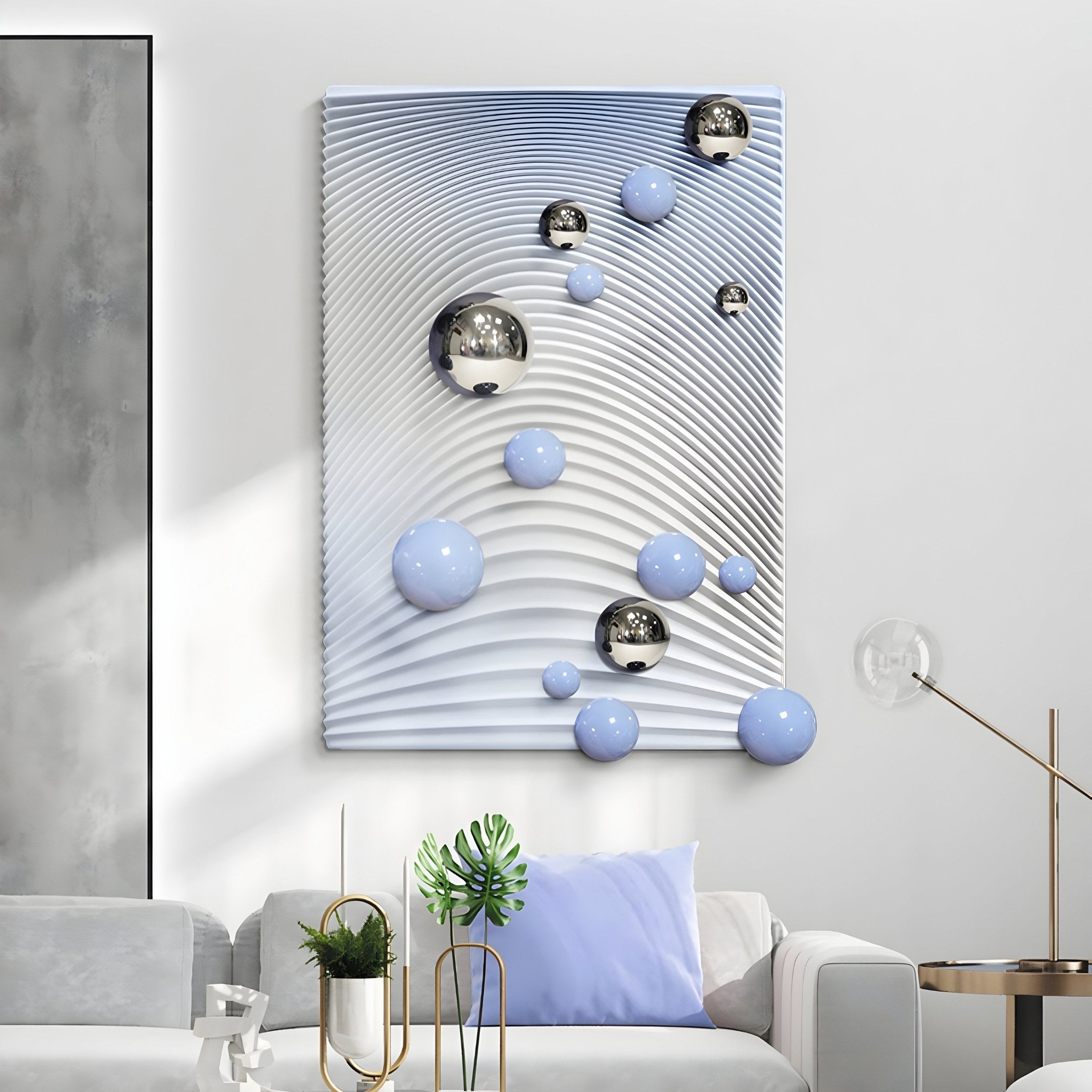 A modern living room features the Sphera Gradient 3D Wood Relief Wall Art by Giant Sculptures, showcasing a wavy white pattern and silver and blue metal spheres. The couch has light gray and blue cushions, while a small side table holds a plant and decor items.