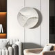 Modern living room with a white tufted sofa and gray armchair features the Selene V White Sandstone Textured 3D Wood Relief Wall Art by Giant Sculptures in soft gray and white tones. Warm lighting and a partially visible shelf to the left complete the minimalist setting.