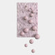 The Fluxion Soft Pink 3D Wood Relief Wall Art by Giant Sculptures features a rectangular, textured panel with wavy lines and glossy pastel pink metal balls in varying sizes—some extending past the edge onto a white background.