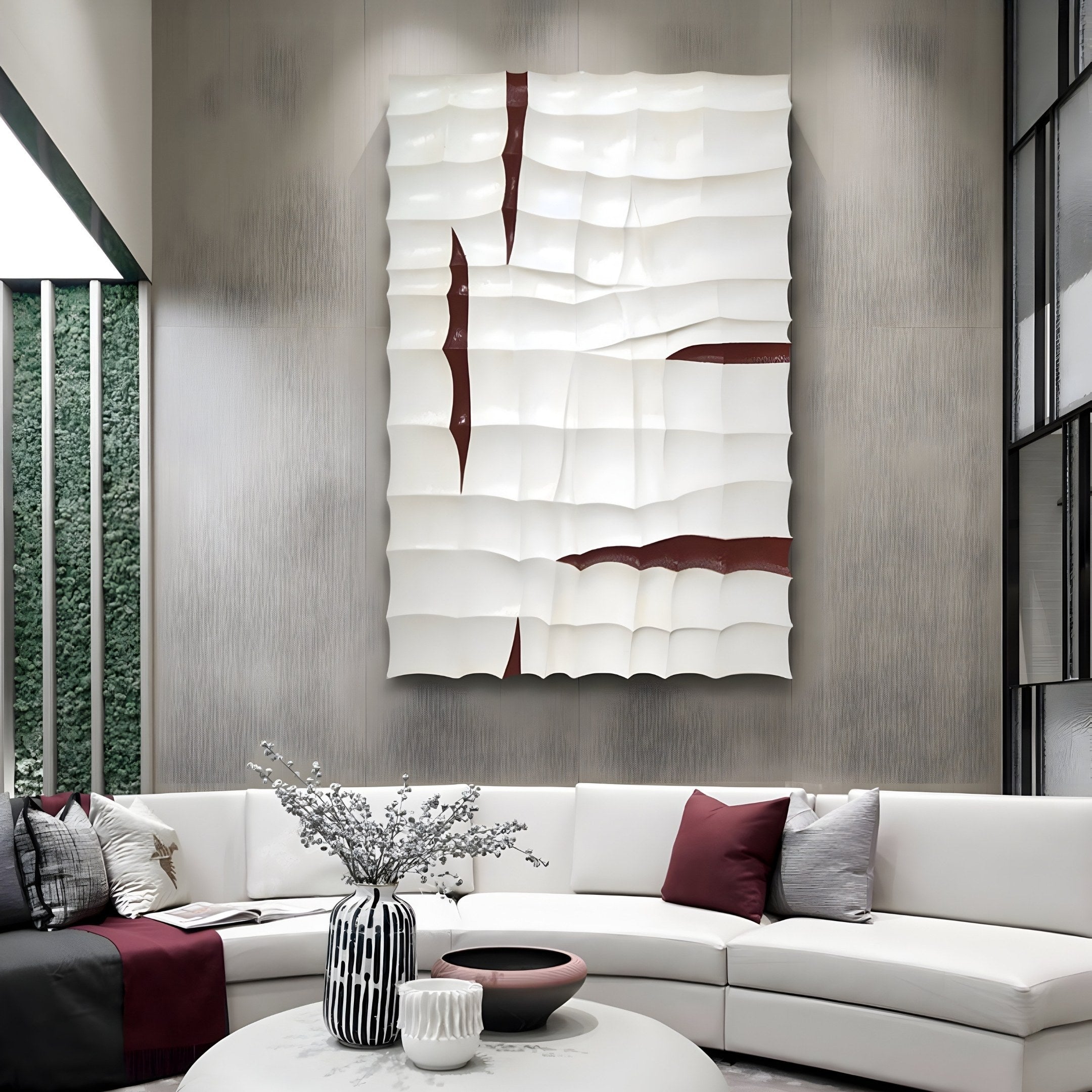 A modern living room showcases a curved white sofa with burgundy and gray cushions, enhanced by the Striata White & Burgundy Wood Carving 3D Wall Art from Giant Sculptures above it. A striped vase with branches and a dark bowl adorn the table against neutral gray walls.