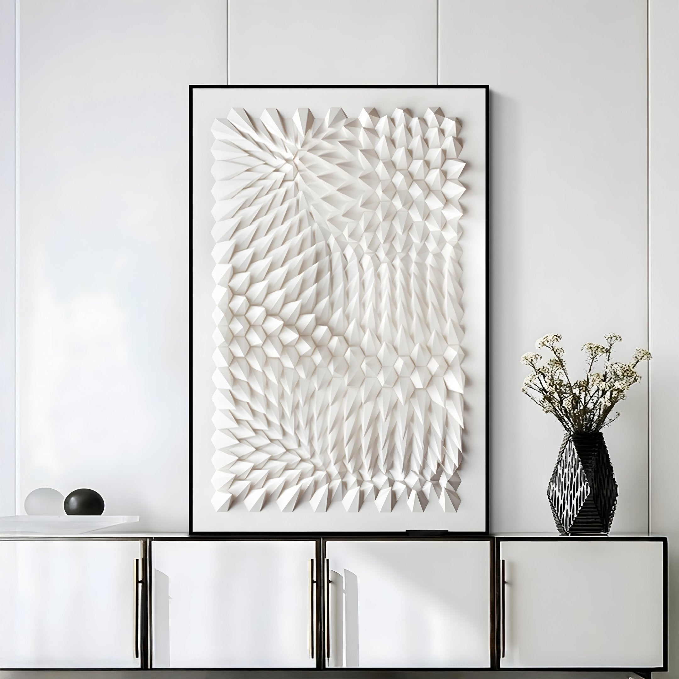 Giant Sculptures Elorium White Strata Hand-Painted Wood Relief 3D Wall Art, with geometric designs, is mounted above a white cabinet. A black vase holding small white flowers sits next to a decorative black and white item, enhancing the rooms depth and style.
