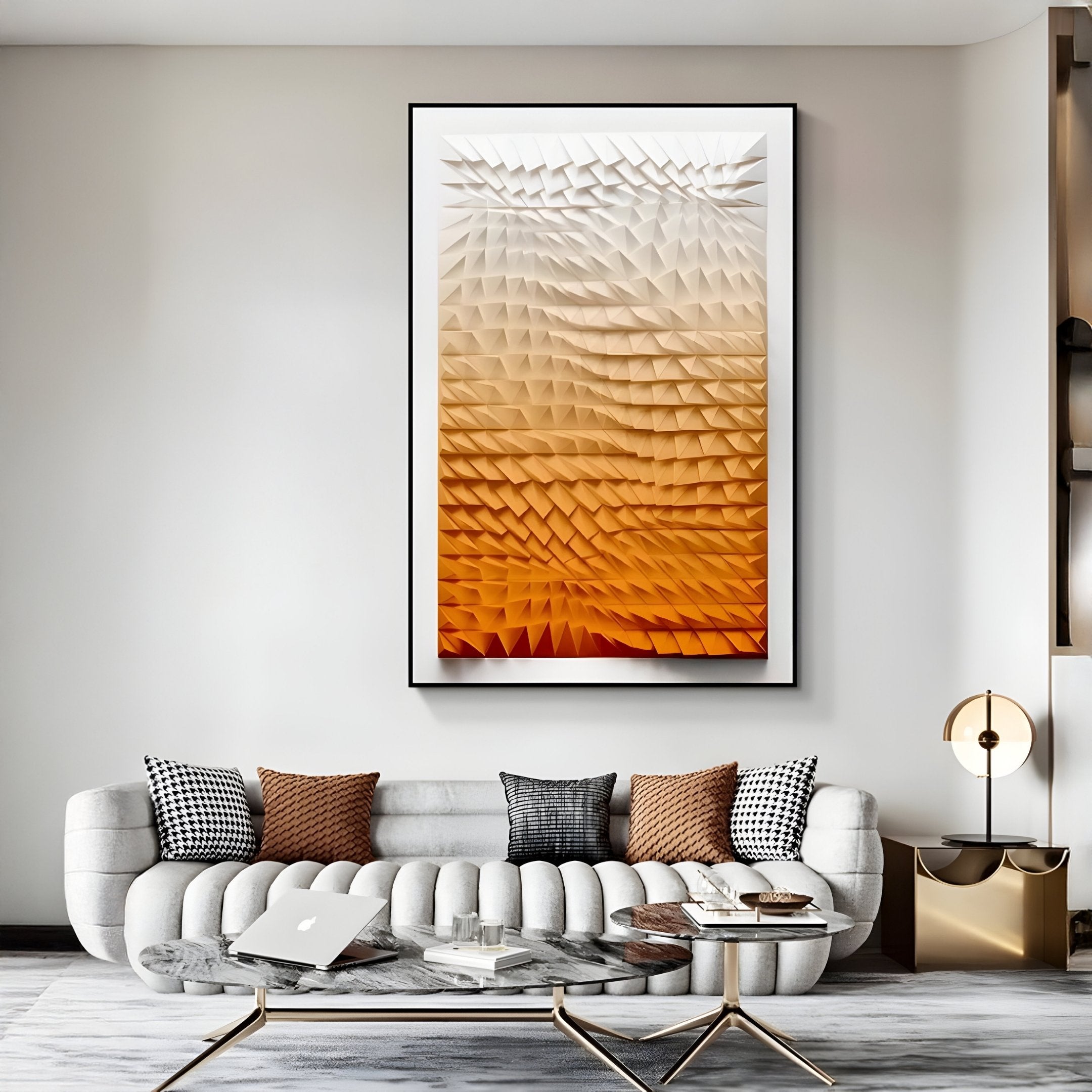 A modern living room features a large abstract artwork from Giant Sculptures—the Elorium Orange Gradient Hand-Painted Wood Relief 3D Wall Art. It includes a curved gray sofa, assorted pillows, a laptop on a small table, and a gold lamp with a circular base for stylish comfort.