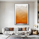 A modern living room features a large abstract artwork from Giant Sculptures—the Elorium Orange Gradient Hand-Painted Wood Relief 3D Wall Art. It includes a curved gray sofa, assorted pillows, a laptop on a small table, and a gold lamp with a circular base for stylish comfort.