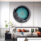 In a modern living room, the Auroria Dynamic Fusion Hand-Painted Wood Relief 3D Wall Art by Giant Sculptures, resembling an eye with a blue-green iris and stone-like textures, graces the wall. Below, a sleek black and white sofa with orange and gray cushions complements the minimalist tables decor.
