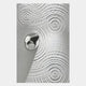 A metallic, irregular object rests on a textured surface with concentric ripples, reminiscent of Giant Sculptures Ondella Silver Ripple III Sandstone Wood Relief 3D Wall Art, in gleaming silver and white tones for a modern, abstract look.