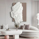 A modern living room exudes contemporary style with the Giant Sculptures Veritas White & Taupe Wood Relief 3D Wall Art, a large abstract sculpture on a beige panel. The space includes a curved white sofa, vases with dried flowers, and soft textured cushions for an inviting touch.