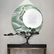 A minimalist display showcases a bonsai on a sleek table, set against Giant Sculptures’ Reveria Sage Green Abstract Wood Carving 3D Wall Art with marbled textures and a white disc—ideal for modern interiors.