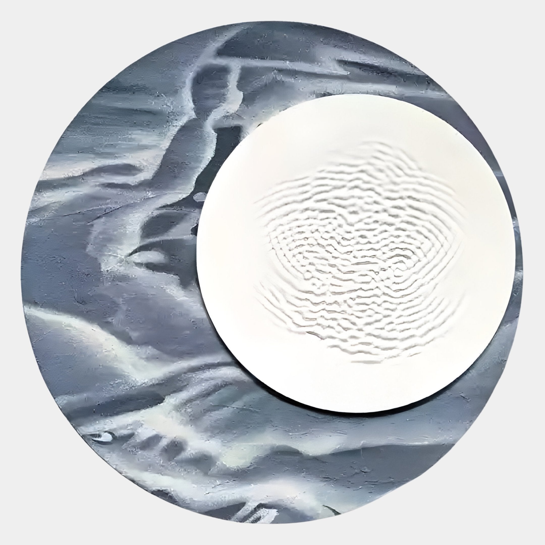 The Reveria Midnight Blue Abstract Wood Carving 3D Wall Art by Giant Sculptures features moody blue and gray wavy patterns, resembling water or marble, as the backdrop for a round white plate with raised concentric designs.