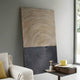 The Artura Beige & Black Hand-Painted 3D Relief Wall Art by Giant Sculptures, featuring concentric ridges, leans against a light gray wall near a window beside a beige sofa and a small table with books and a yellow box.