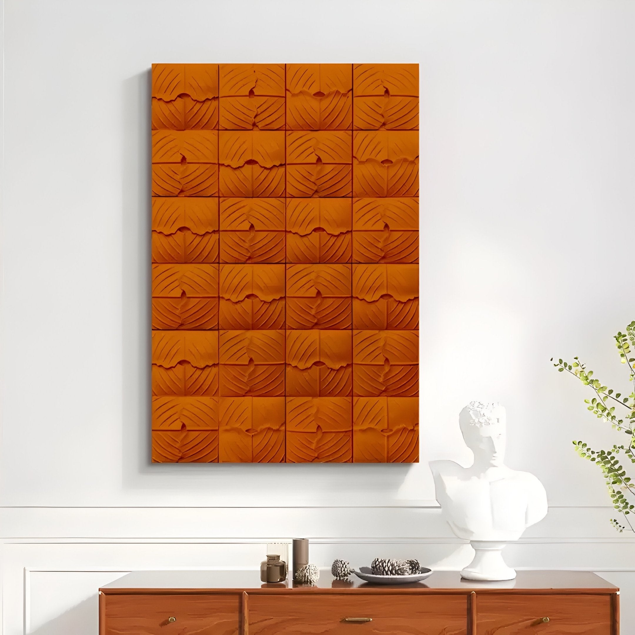 The Vellura Orange Textured Wood Relief 3D Wall Art by Giant Sculptures hangs above a wood cabinet topped with a white bust sculpture and a glass vase holding green foliage.