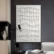 A modern room showcases the Novara White I Hand-Painted Wood Relief 3D Wall Art by Giant Sculptures, featuring black wood grain-like patterns. Nearby are a black desk lamp and chair, a geometric vase on a shelf, and part of a gray sofa.