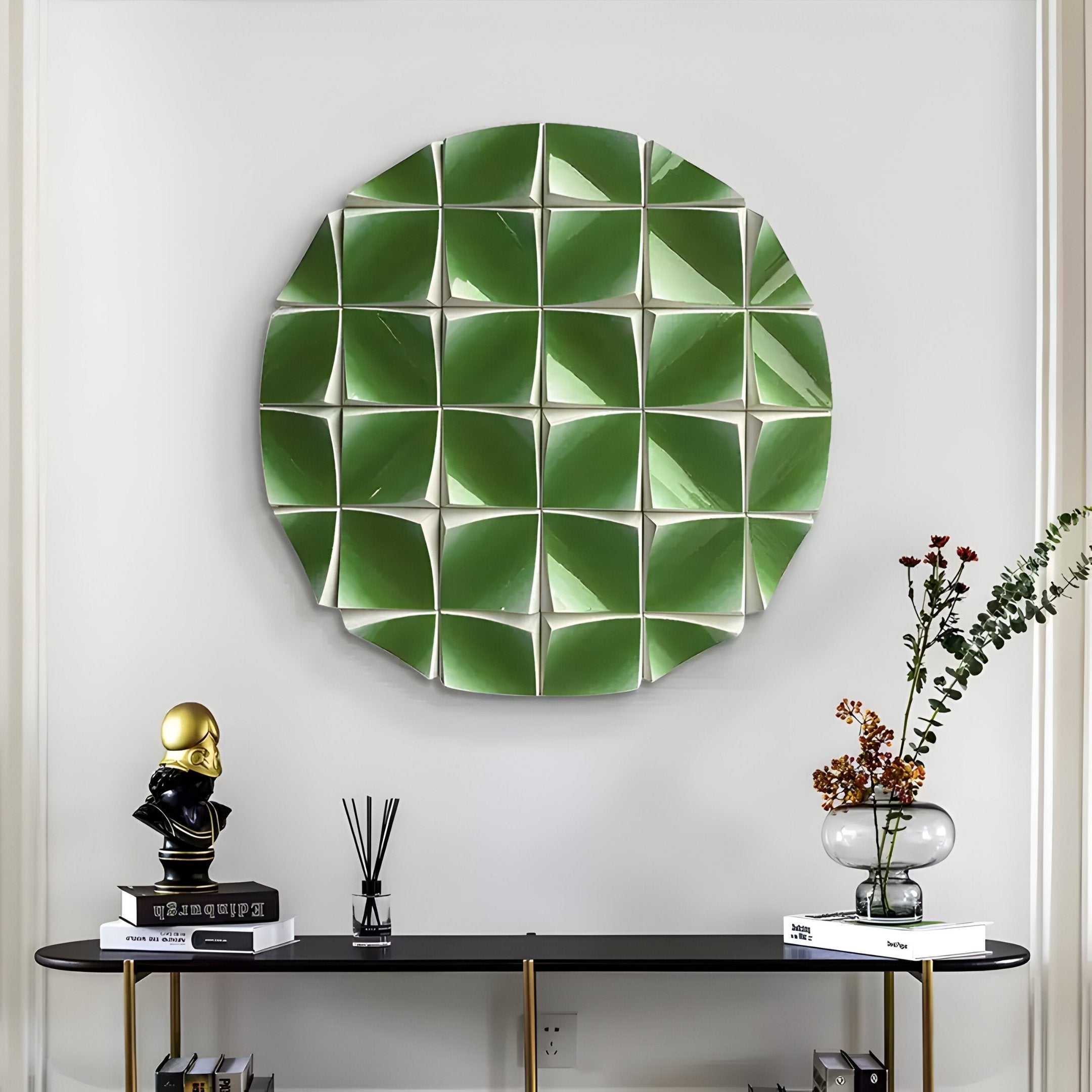 The Incalia Green Circular Geometric Wood Relief 3D Wall Art by Giant Sculptures, featuring a green and white folded pattern, hangs above a black console table adorned with books, a gold and black bust, flowers in a glass vase, and a reed diffuser.