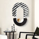 The Arcus Black & White Zebra Stripes Mirror 3D Wooden Wall Art by Giant Sculptures features a semicircular design with zebra stripes on top and a textured bottom. Below, a small shelf holds decorative dried grasses. Nearby, theres a table with candles and a bowl, plus a black chair in view.