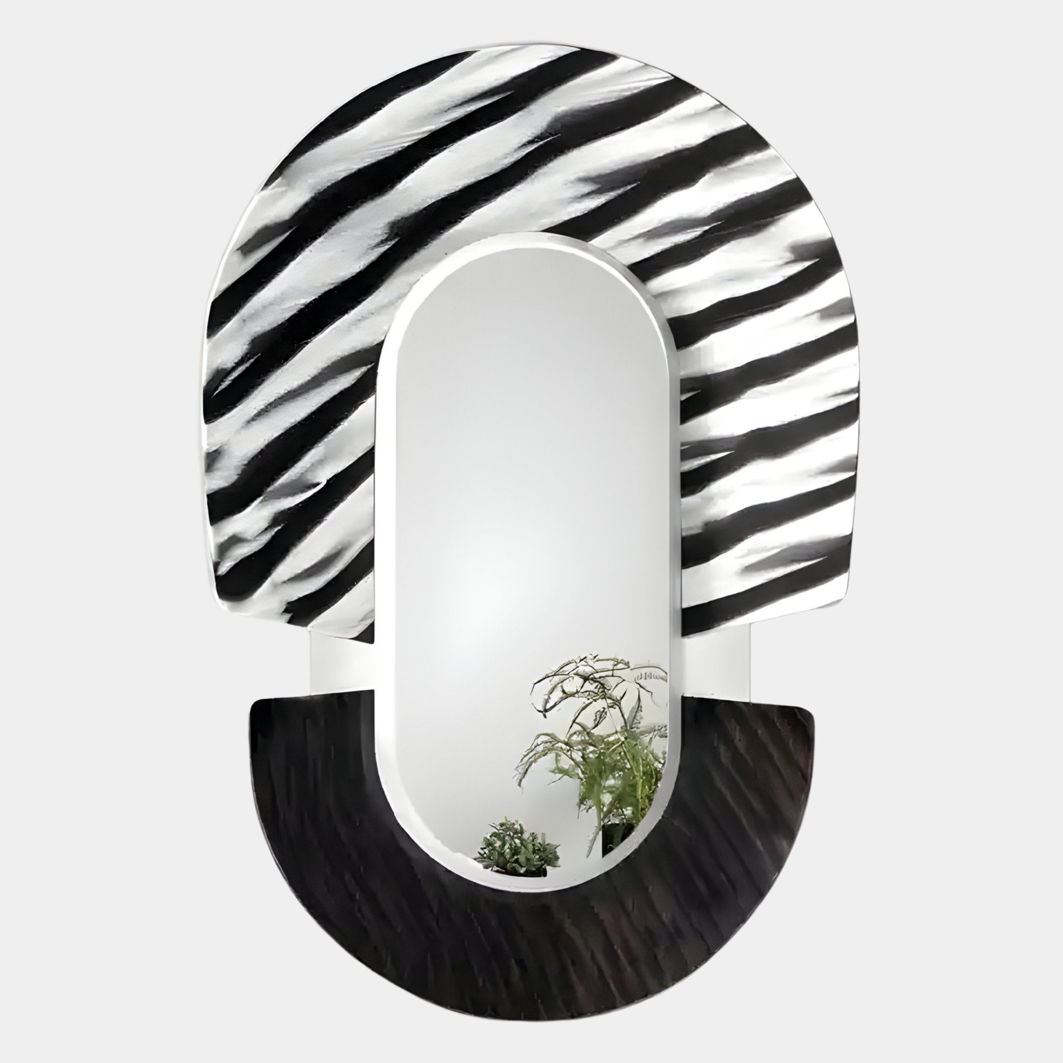The Arcus Black & White Zebra Stripes Mirror 3D Wooden Wall Art by Giant Sculptures features a bold black and white striped top, a solid textured black bottom, and reflects green leafy plants—perfect as distinctive contemporary décor.