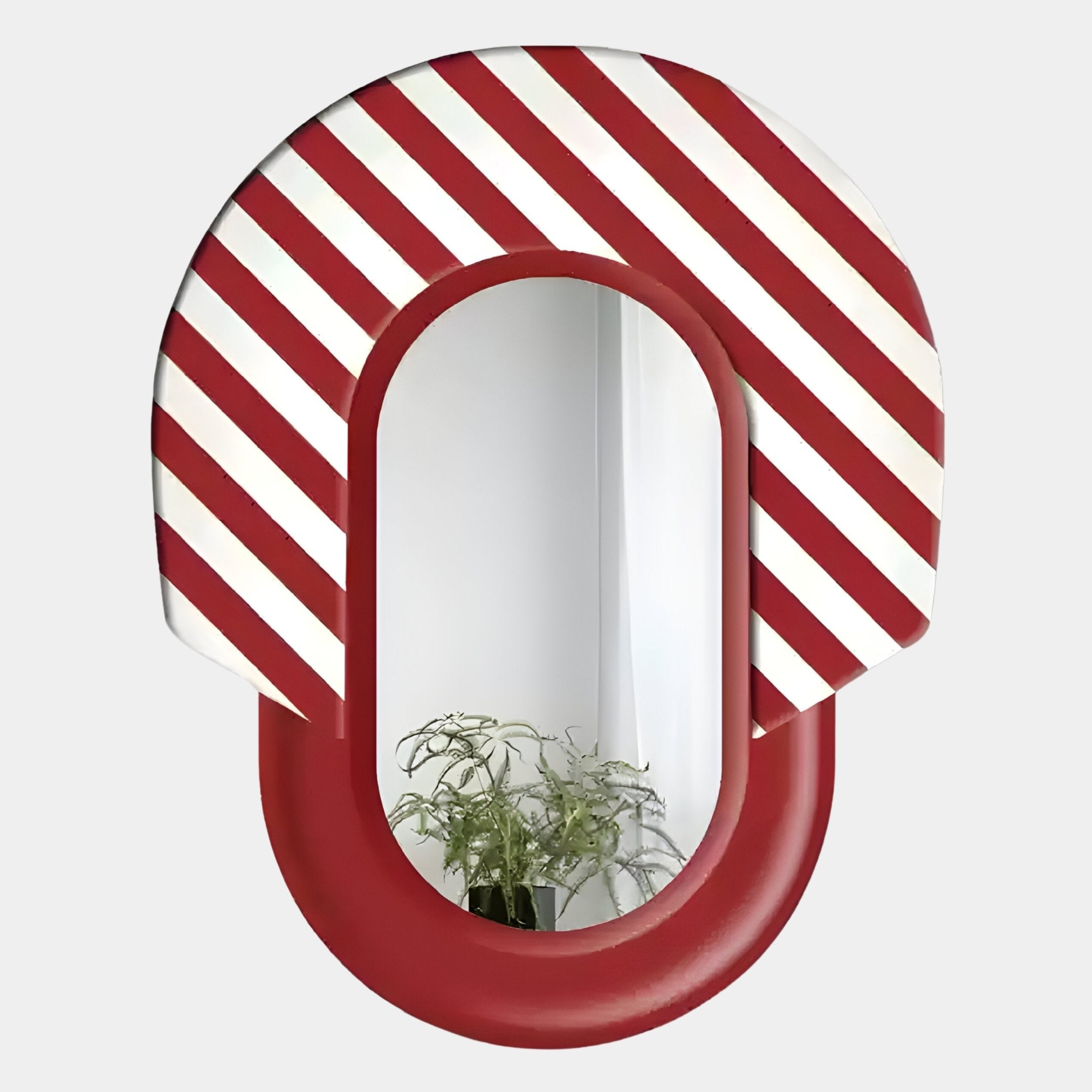 The Arcus Red & White Striped Mirror 3D Wooden Wall Art by Giant Sculptures features a bold oval frame with vivid diagonal stripes, reflecting a potted plant and crisp white walls in the background.
