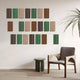 A modern, minimalist room includes a wooden chair and small green table, enhanced by nature-inspired decor. The Eximia Brown & Green Tones Multi-Panel Wood Relief 3D Wall Art by Giant Sculptures adds depth with its geometric design, while a tall plant peeks from the right.