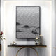 A modern interior features a decorative black console table with a lantern, potted plant, and small sculpture. Above it hangs the Synova Silver II Hand-Painted Wood Relief 3D Wall Art by Giant Sculptures, with textured abstract patterns resembling a zen-inspired landscape on the white wall.