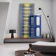 A modern, minimalist room showcases the Lineris Blue Glossy Wood Relief 3D Wall Art by Giant Sculptures featuring abstract blue and yellow vertical shapes. A sculptural decor sits on a low platform with a sleek black lamp, while a curved floor lamp elegantly arches over the serene space.
