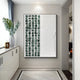 A modern interior features the Aestilis Green & White Mosaic Wood Carving 3D Wall Art by Giant Sculptures with a green stone grid on the left and white design on the right, a vase with greenery on a cabinet beneath a window, and visually interesting hand-carved wood flooring.