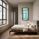 A modern bedroom with a large window, wooden floor, light bedding, neutral walls, and the Lumiscale Black & Blue Modular Glass Wall Mirror by Giant Sculptures to enhance light and complement the contemporary decor.