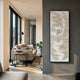 A modern living room features a beige sofa, black floor lamp, small black side table with books, potted plant, and the Auravolta I Pearl Beads Swirl Pattern 3D Wall Art by Giant Sculptures on a gray wall as sunlight streams through large windows.