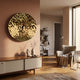 A modern living room features the Giant Sculptures Lumineris Gold Ripple Sphere Metal 3D Wall Art above a wooden sideboard, a cozy beige armchair with a throw blanket, a floor lamp, bookshelves, and soft natural light from a tall window.