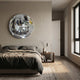 A modern bedroom with neutral tones features the Giant Sculptures Lumineris Silver Hexa-Mirror Circular Metal 3D Wall Art above a gray-bedded bed, a wooden nightstand with lamp, and a window letting in natural light.