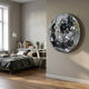 A modern bedroom with wooden floors, gray bedding, a desk with books and a plant, and Giant Sculptures' Lumineris Silver Facet Matrix Circular Metal 3D Wall Art on the beige wall reflecting light.