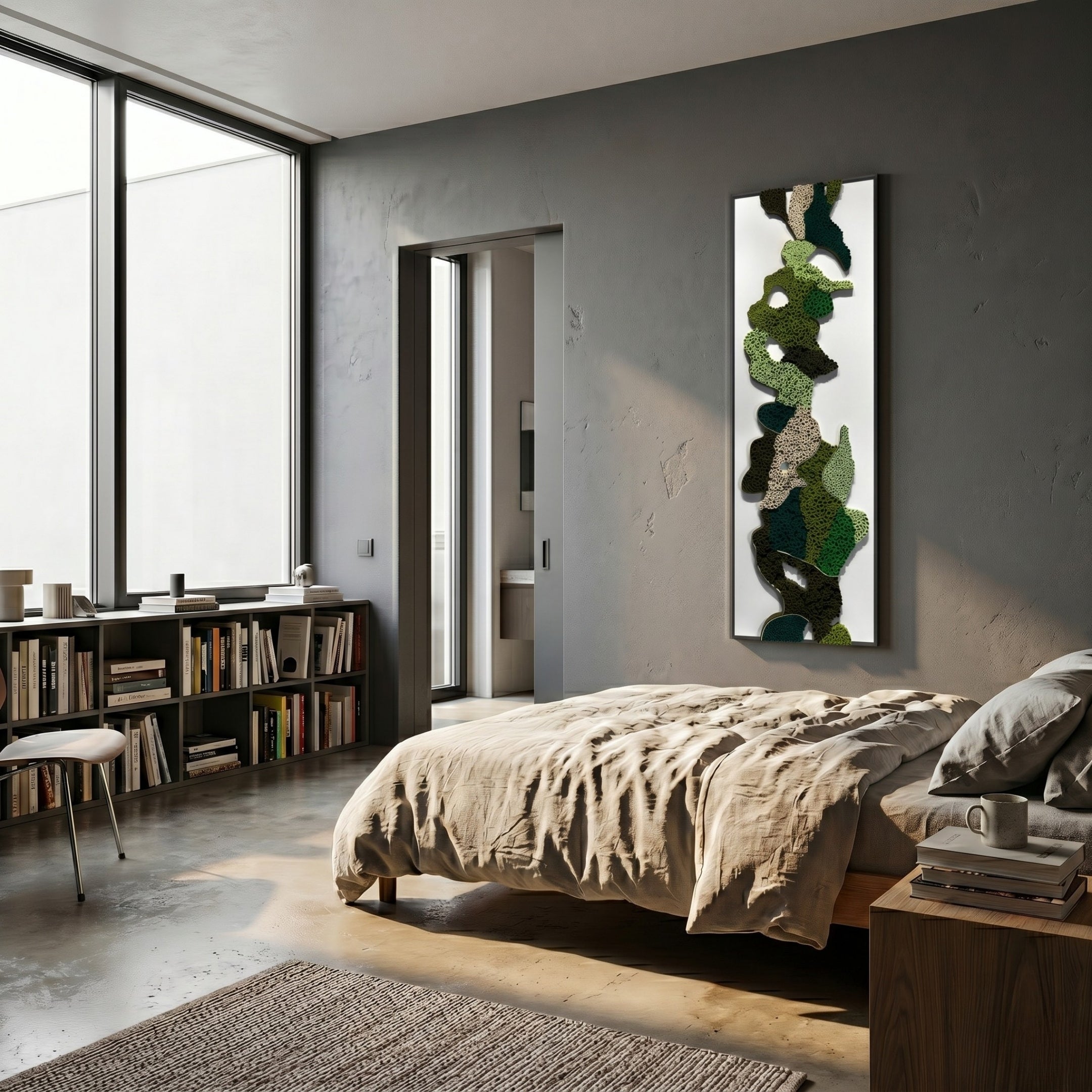 A modern bedroom with a large window, neatly made bed, low bookshelf of books, chair, and the Verdurelle Green Layered Flow Felt 3D Wall Art by Giant Sculptures adds abstract green flair to the gray wall. Natural light fills this minimalist space.