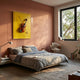 A cozy modern bedroom with a low bed in gray bedding, a large window, and Giant Sculptures' Archetto Yellow Violin Acrylic Framed 3D Wall Art mounted above the bed on a pinkish wall, illuminated by natural light.