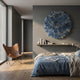 Rivora Blue Ribbon Leather Circular 3D Wall Art by Giant Sculptures mounted on a grey bedroom wall above a shelf, beside a leather butterfly chair and bed.