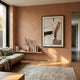 A modern living room with a light brown accent wall, Bravura III Stroke Abstract Framed Canvas Wall Art by Giant Sculptures, a low wooden bench with books and a vase, large windows, a neutral rug, and soft natural light for minimalist interiors.