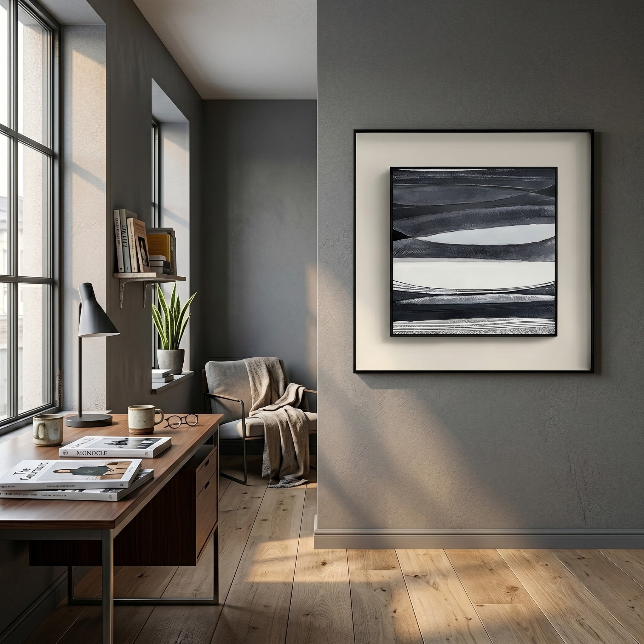 A modern home office features a wooden desk, books, coffee mug, lamp, and potted plant by a large window. An armchair with a blanket sits nearby. Stratonis Monochrome Layered Textured Framed Wall Art by Giant Sculptures decorates the gray wall.