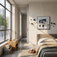 A modern bedroom features a neatly made bed, nightstand with lamp and books, shoes on the floor, large windows with scenic views, and the Aeroluxe Navy Crest Abstract 3D Wall Art With Metal Balls by Giant Sculptures as striking decor.