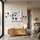 A modern living space with a light wood console, a white vase with twigs, and the Aeroluxe Navy & White Abstract 3D Wall Art With Metal Balls by Giant Sculptures. Large windows reveal a cozy bedroom in the background.